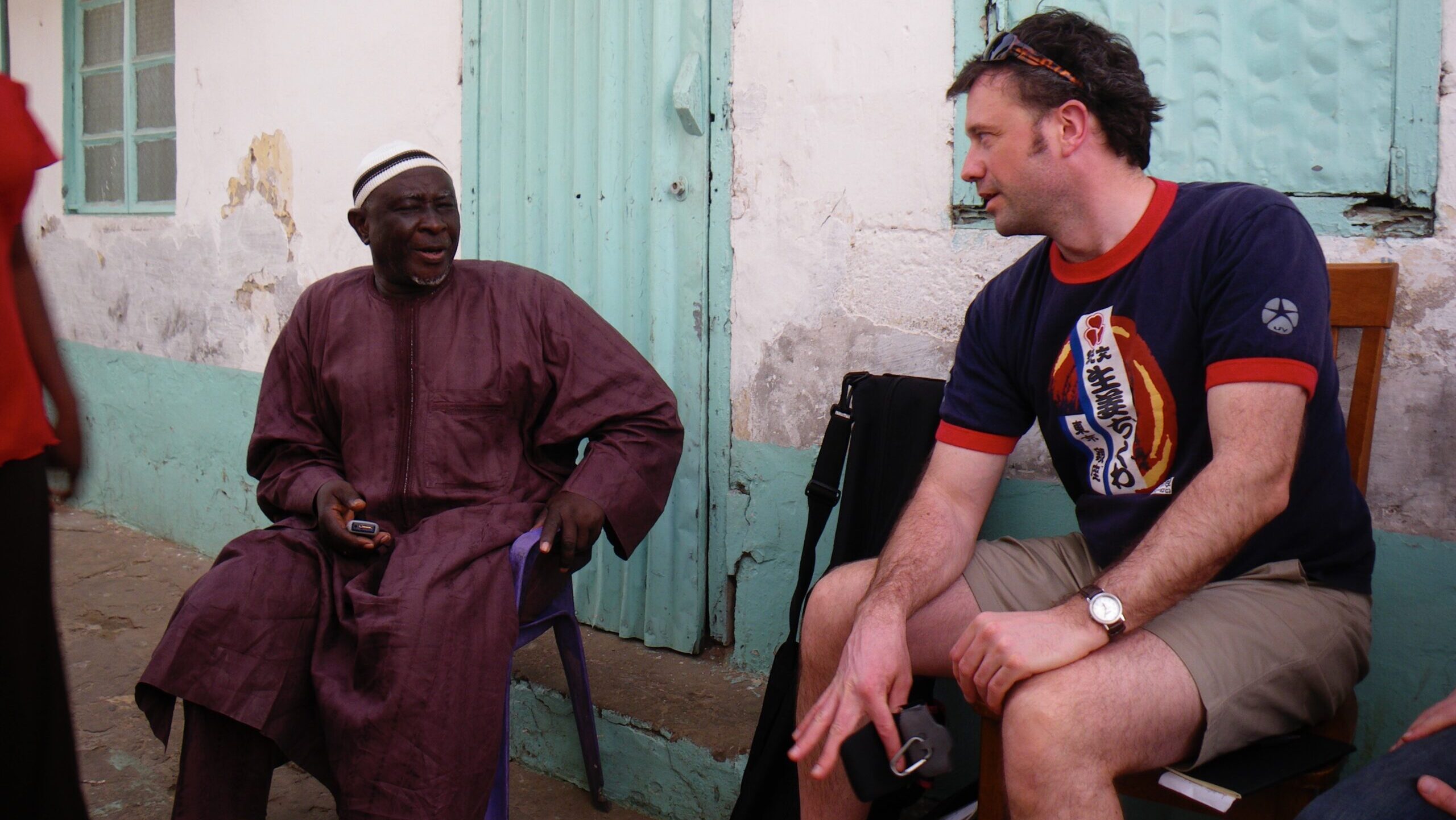 two men sit in conversation, a Gambian man and a Canadian man